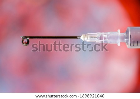 Hypodermic needle dripping fluid over a red and grey out of focus background