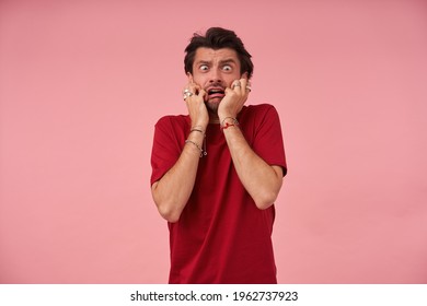 Hysrerical crazy young man with stubble in red tshirt feels terrified and looks panicked over pink background
