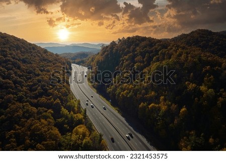 I-40 freeway road leading to Asheville in North Carolina thru Appalachian mountains with yellow fall forest and fast moving trucks and cars. Concept of high speed interstate transportation