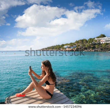 Ibiza girl taking smartphone photos at Portinatx beach  pier in Balearic Islands