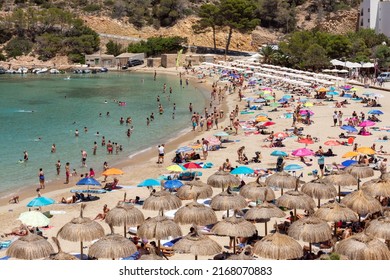 Ibiza - Spain. July 05, 2021: Adults And Children Sunbathe On White Sand Of Cala Vedella Beach In Ibiza, Swim In Shallow Crystal Sea Water Of Cove. Balearic Islands, Spain