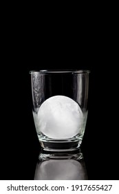 Ice Ball Inside Cocktail Glass On A Reflective Black Table.