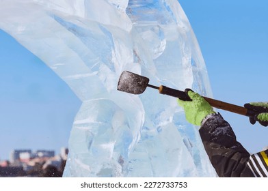 An ice block is carved with a chisel in the hands of a sculptor on a sunny winter day. The master works with a homemade cutting tool. Close up. - Powered by Shutterstock