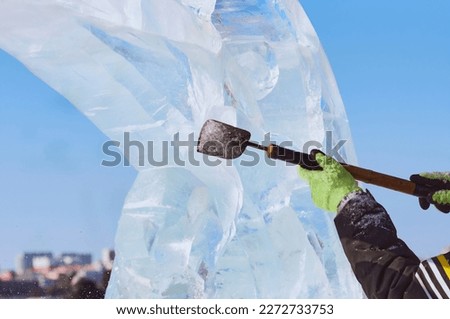 An ice block is carved with a chisel in the hands of a sculptor on a sunny winter day. The master works with a homemade cutting tool. Close up.