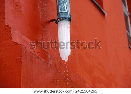 Ice block thaw in rain gutter. Gutter downspout with melting ice. Icicles melt in gutter. Winter ice melt in drain system. Icy drain pipes on facade of the building. Drain pipe with ice