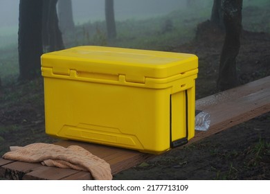 Caja de hielo refrigerador móvil Se colocó un refrigerador amarillo en un banco de madera en el bosque nublado para equipos de camping.