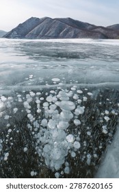 Ice bubbles are visible beneath the surface of a frozen lake, with snow-covered mountains rising in the background under a clear sky