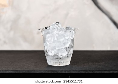 A ice bucket filled with cubes of ice sitting on a black textured table - Powered by Shutterstock