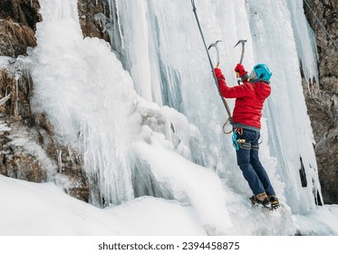 Ice climber dressed in warm winter climbing clothes, safety harness and helmet climbing frozen waterfall using two Ice climbing axes and crampons. Active people and sports activities concept image. - Powered by Shutterstock