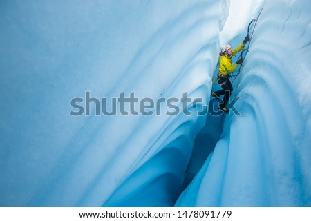 Ice climber lowered into narrow ice canyon on the Matanuska Glacier. He climbs between walls of strange wavy patterns in the ice carved by a river of melt water.