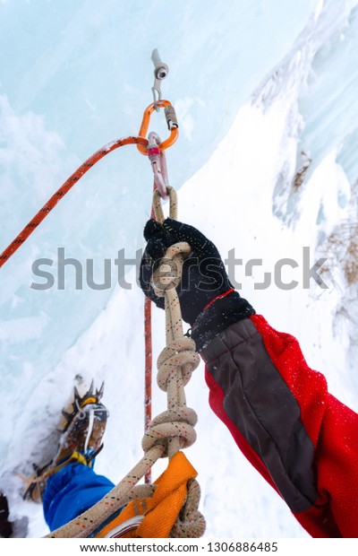 Ice climbing anchor with ice\
screw, safety rope, carabiners and climber`s arm,\
closeup