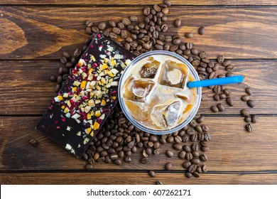 Ice Coffee With Milk In Takeaway Cup, Chocolate Bar And Coffee Beans On Wooden Background. Top View.