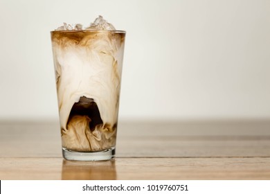 Ice Coffee On A Wood Table With Cream Being Poured Into It Showing The Texture And Refreshing Look Of The Drink, With A Clean Background.