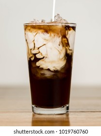 Ice Coffee On A Wood Table With Cream Being Poured Into It Showing The Texture And Refreshing Look Of The Drink, With A Clean Background.