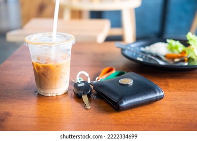 Ice Coffee In Plastic Glass With Wallet And Car Keys On Wood Table In Cafe