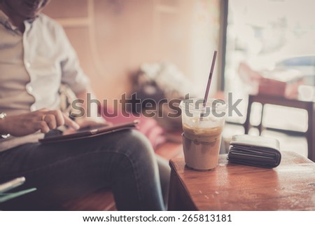 Ice coffee in plastic glass with wallet in cafe with businessman  using tablet background.