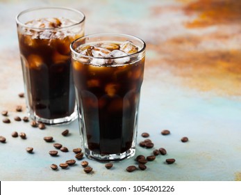 Ice coffee in a tall glass with cream poured over and coffee beans. Cold summer drink on a blue rusty background with copy space
