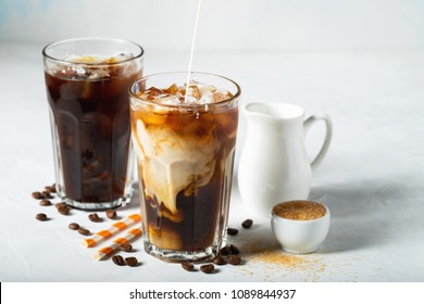 Ice Coffee In A Tall Glass With Cream Poured Over And Coffee Beans. Cold Summer Drink On A Light Blue Background