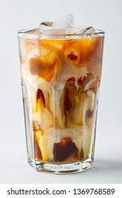Ice coffee in a tall glass with cream poured over and coffee beans. Cold summer drink on a light background