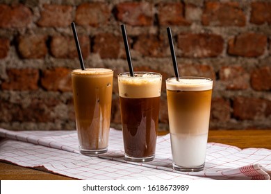 Ice coffee in a tall glass with cream poured over on a old rustic wooden table. Cold summer drink with tubes on a rustic background with copy space.