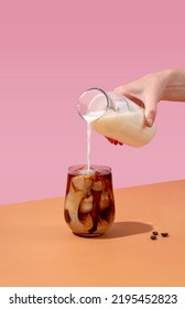 Ice coffee in a tall glass with cream poured over and coffee beans. A woman's hand pours cream into a glass of coffee. - Shutterstock ID 2195452823