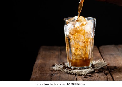 Ice coffee in a tall glass over and coffee beans on a old rustic wooden table. Cold summer drink on a dark background with copy space. The process of pouring drink from a coffee pot into a glass - Shutterstock ID 1079889836