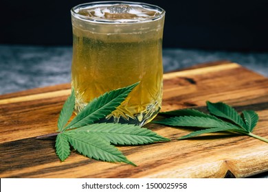 Ice cold Marijuana cannabis infused drink in a crystal clear glass with weed leaves on a dark wood background