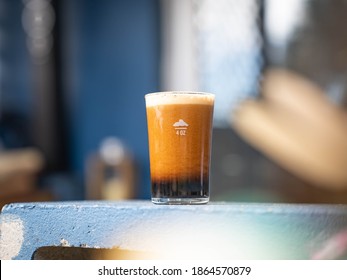 Ice Cold Nitro Dispensed Glass Of Dark Beer With Foam Outside On A Sunny Day. Stout Beer Freshly Poured With Big Head On Blue Shelf. 