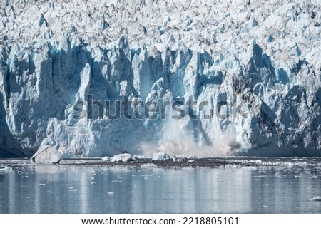 Ice collapses from the edge of a high glacier and splashes into the sea.  Water sprays upwards.