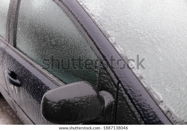 Ice covered car side glass with mirror,\
windscreen and side door, close up front side view of an icy\
vehicle on a winter day after freezing rain in\
Russia