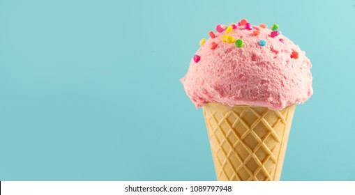 Ice cream cone close-up. Pink Icecream scoop in waffle cone over blue background. Strawberry or raspberry flavor Sweet dessert decorated with colorful sprinkles, closeup