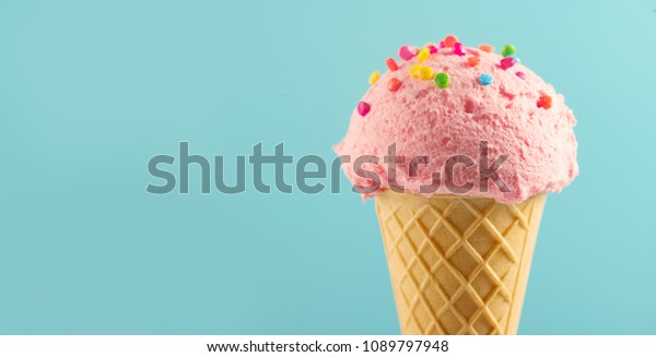 Ice cream cone close-up.\
Pink Icecream scoop in waffle cone over blue background. Strawberry\
or raspberry flavor Sweet dessert decorated with colorful\
sprinkles, closeup