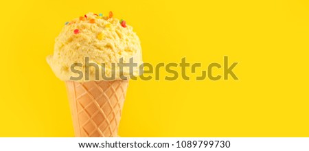 Ice cream cone close-up. Yellow Icecream scoop in waffle cone over yellow background. Banana, Vanilla or Lemon flavor Sweet dessert decorated with colorful sprinkles, closeup