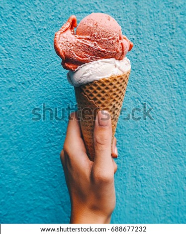 Ice cream cone on a blue background. The woman holding the ice cream by hand.