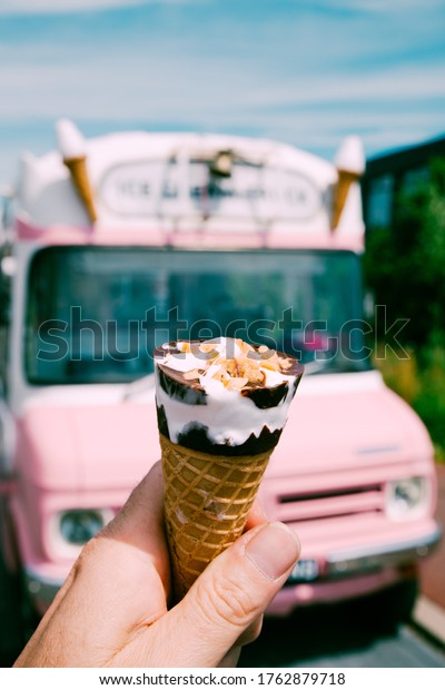 Ice cream cone with a pink ice cream truck or\
van in the background.
