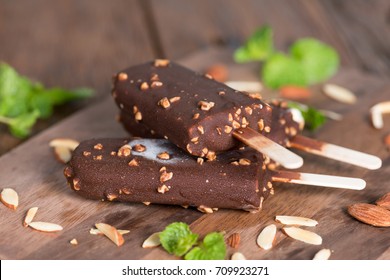 Ice cream covered with chocolate and almonds sticks frozen on wood board. Popsicle and Lolly sweet dessert.