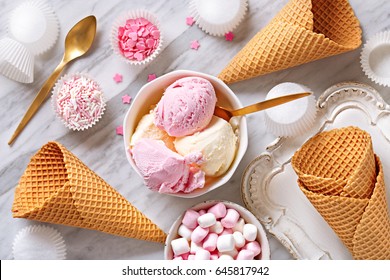 Ice cream ingredients view from above on a marble background. Ice cream in a bowl, ice cream cones, spoon, marshmallows, cupcake papers. Top view.