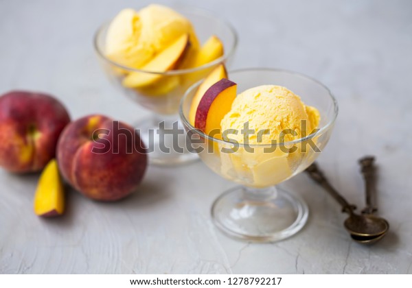 Ice cream\
with peaches in cups on concrete background. Tasty summer\
refreshing dessert. Fruits ice cream\
scoops