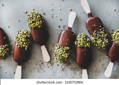 Ice cream popsicle pattern. Flat-lay of chocolate glazed ice cream pops with pistachio icing over grey concrete background, top view, close-up. Summer seasonal cold sweet healthy vegan dessert