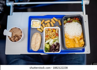 Ice Cream, Rice, Salad, Yellow Sauce, And Pudding On Gray And Blue Tray From Above. Top View Of Fresh Airplane Complete Meal Above Small Table. Plane Food