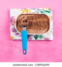 Ice cream scoop in chocolate ice cream tub on napkin on pink background. Square