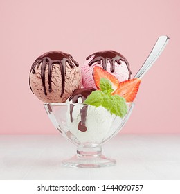 Ice Cream Scoops With Slices Strawberry, Green Mint, Spoon, Chocolate Sauce In Bowl In  Pink  Interior On White Wood Board, Closeup, Square.