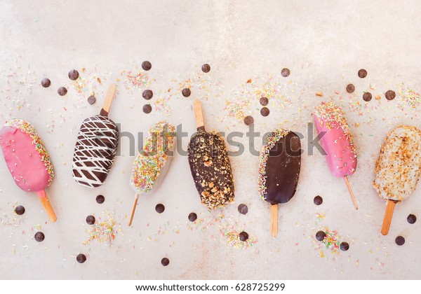 Ice cream sticks with chocolate, fruit, roasted\
almonds and colorful sugar sprinkles on rustic background. Top\
view, blank space