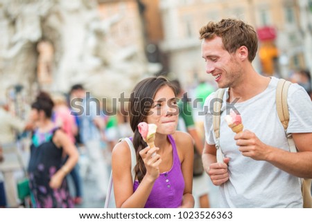 Ice cream summer fun couple eating gelato in Rome on Piazza Navona. Happy people having fun eating ice cream on vacation travel in Italy, Europe. Young funny girl licking lips of italian food outdoor.