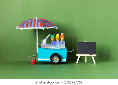 Ice cream toy cart with blue red umbrella. Assortment of ice cream empty menu black chalkboard. Summer vacation concept. Green background