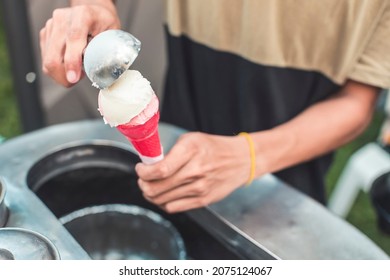 An ice cream vendor places scoops of coconut and strawberry sorbetes into a small wafer cone. Traditional ice cream in the Philippines.