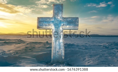 Ice cross in the middle of a frozen lake against the sky .  Christian symbol with a human silhouette inside .