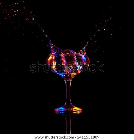 Ice cube falling down into glass with martini cocktail against dark background with neon light. Traditional taste. Concept of alcohol drink, nightclub, party, taste, celebration.
