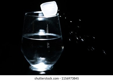 Ice Cube Knocked Off Glass Edge Splashing Away Drops Low Key On Dark Background