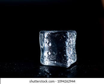  Ice Cube On A Black Background Is Melting With Drops Of Water.